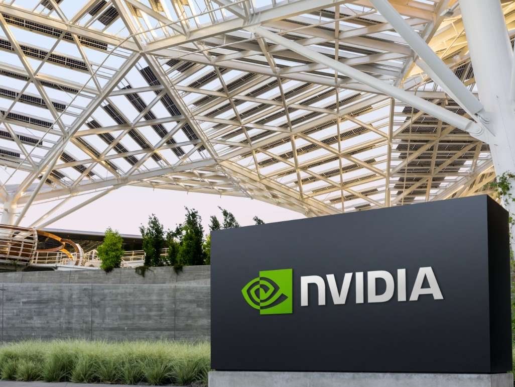 Nvidias logotyp på en mörk skylt framför en byggnad med ett tak av solpaneler, vilket speglar företagets innovation och hållbarhetsfokus.