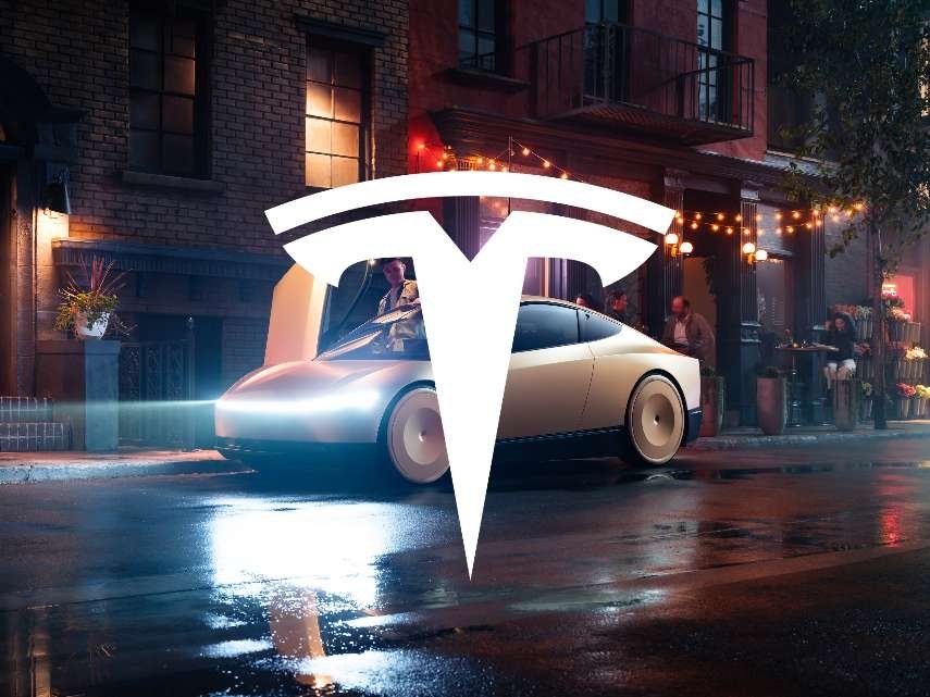 Vitt Tesla-märke över en ljus bil på en våt gata med tegelbyggnader, lampor och människor i bakgrunden.