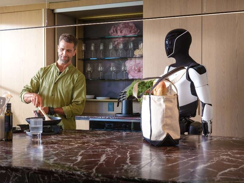 En man lagar mat i ett kök bredvid en svartvit robot och en matkasse.